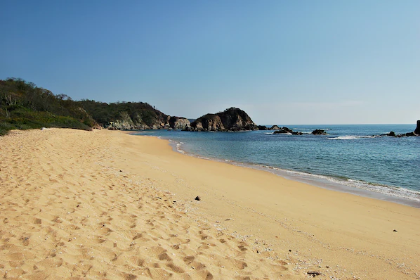 Conejos Bay near Dreams Huatulco Resort & Spa with golden sand beach, clear waters, and rocky Pacific coastline