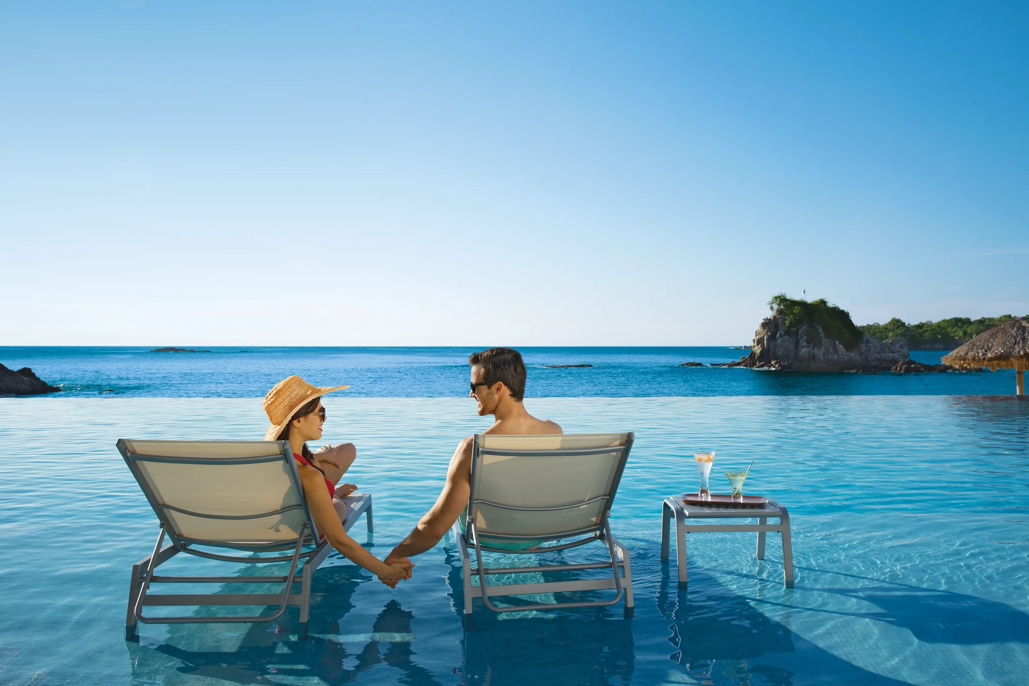 Couple holding hands while relaxing on in-pool loungers at Dreams Huatulco Resort & Spa.
