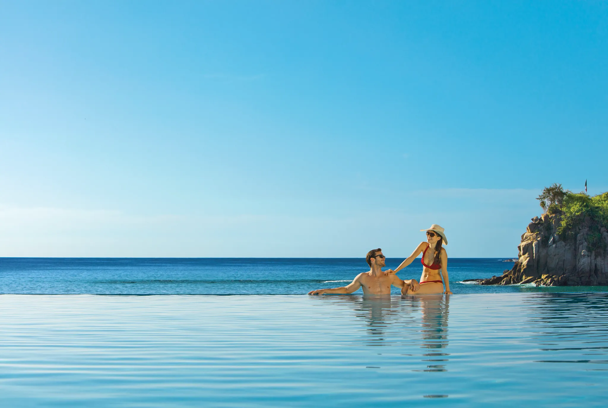 Couple enjoying ocean views while leaning on the infinity pool edge at Dreams Huatulco Resort & Spa.