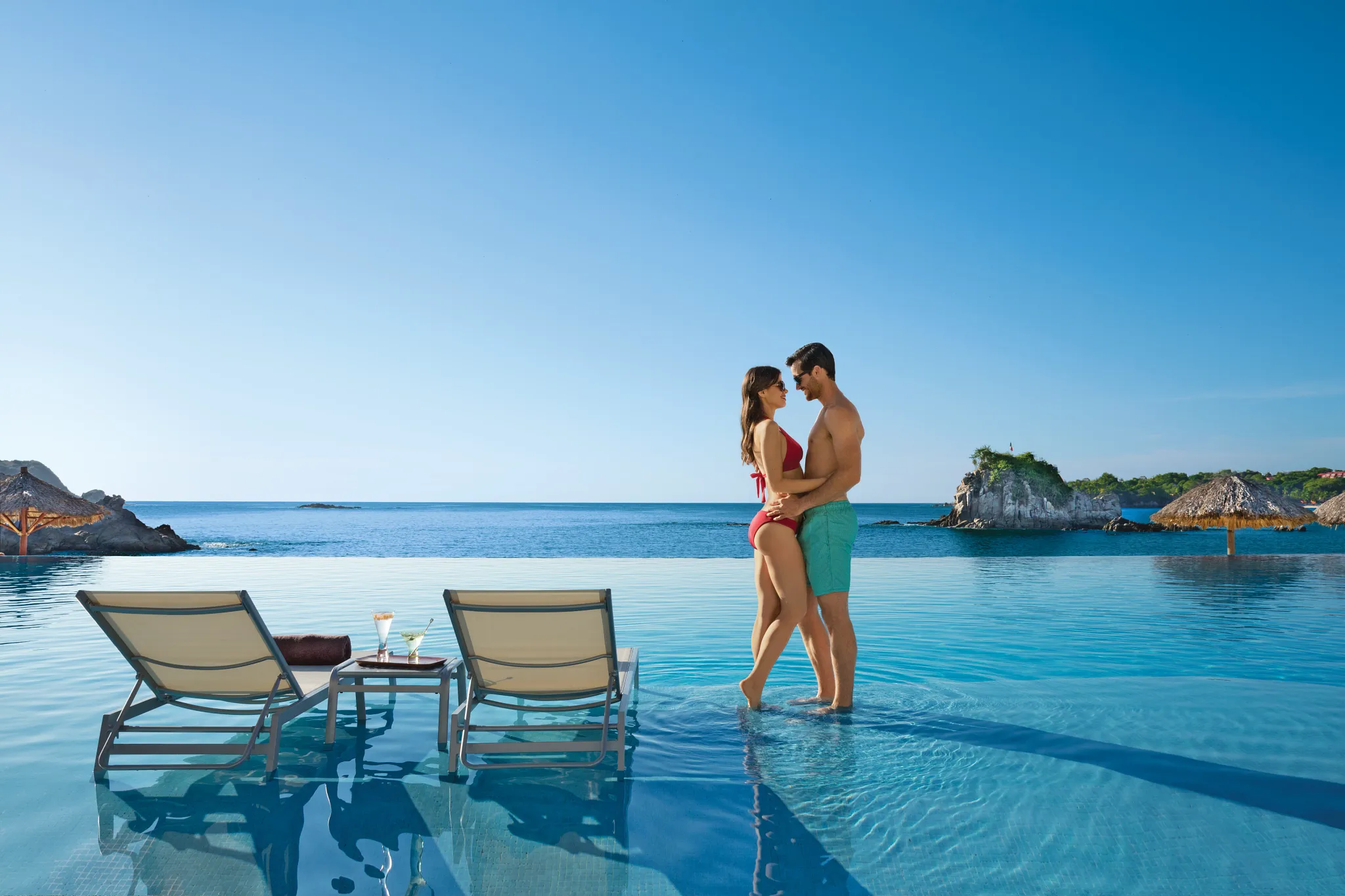 Romantic couple relaxing together at the infinity pool at Dreams Huatulco Resort & Spa, surrounded by ocean views and Huatulco’s natural coastline.