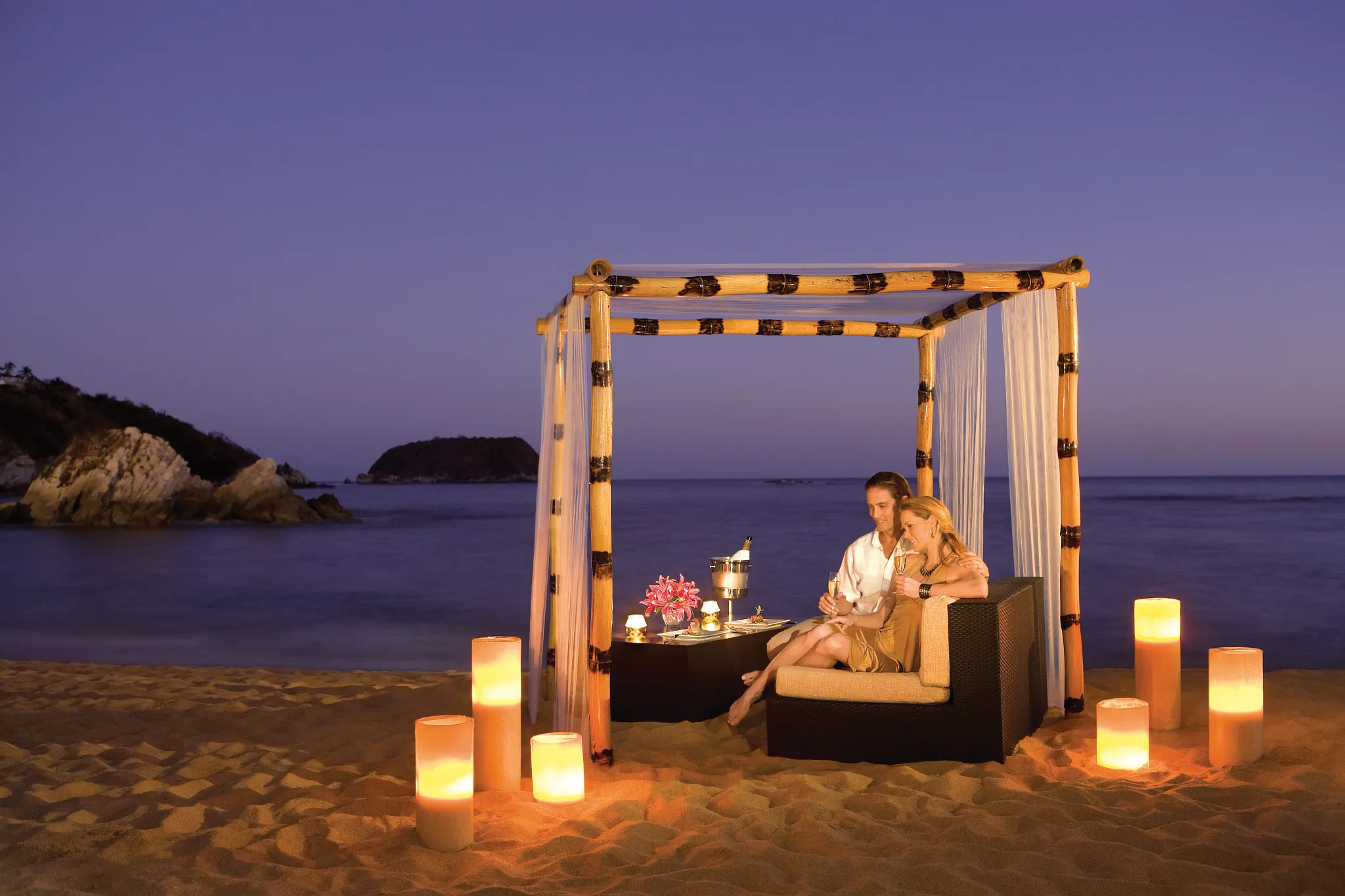 Couple enjoying a private candlelit beach dinner at Dreams Huatulco Resort & Spa at sunset.