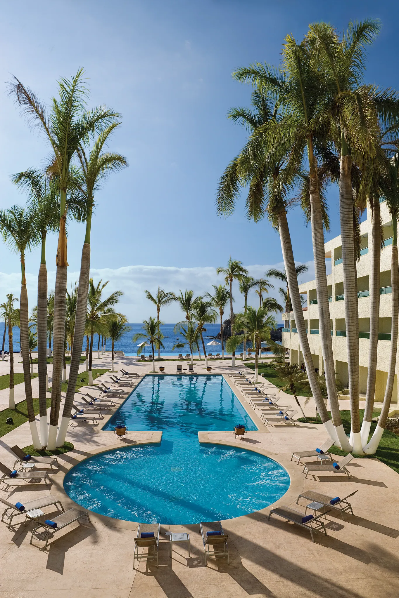 Main pool surrounded by palm trees at Dreams Huatulco Resort & Spa with ocean views in the background.