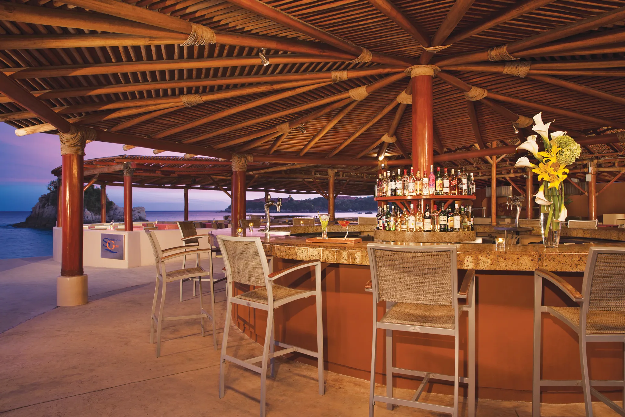 Seaside Grill at Dreams Huatulco Resort & Spa featuring an open-air poolside grill bar, thatched roof, and oceanfront seating.